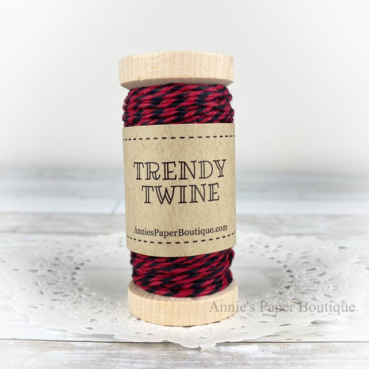 Red and black cotton craft twine wrapped around a wooden spool sitting on a white background.