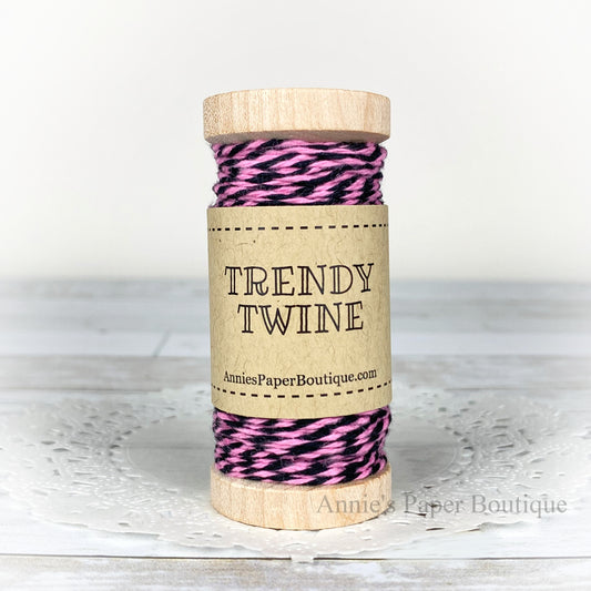 Pink and black cotton craft twine wrapped around a wooden spool sitting on a white background.